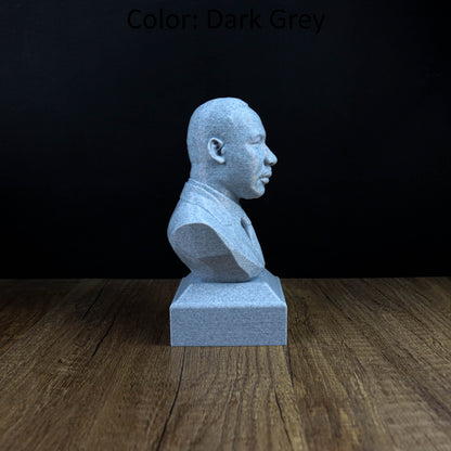 A gray stone bust statue of a man is displayed on a wooden surface against a dark background.