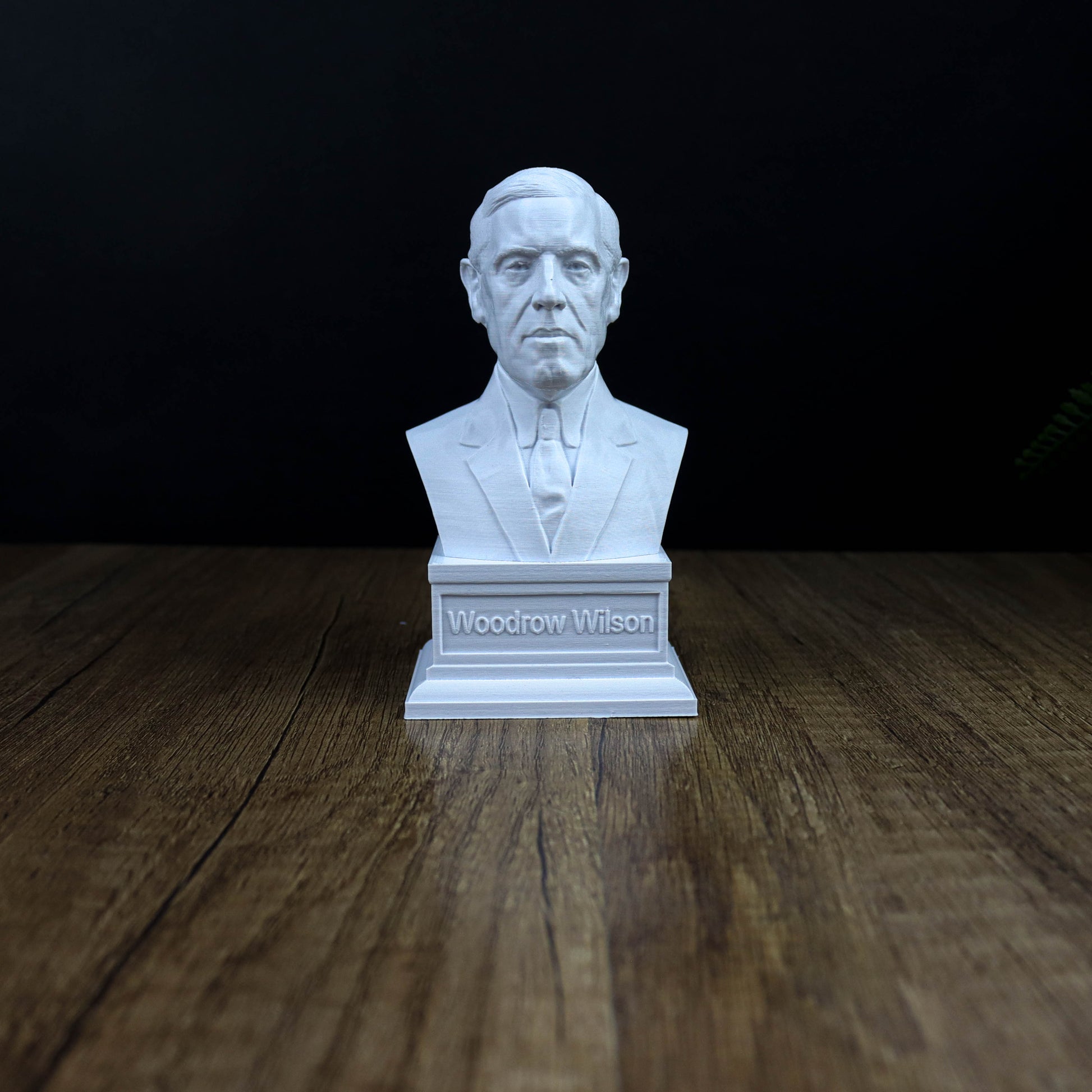 A white bust of a man wearing a suit and tie, sitting on a wooden surface.