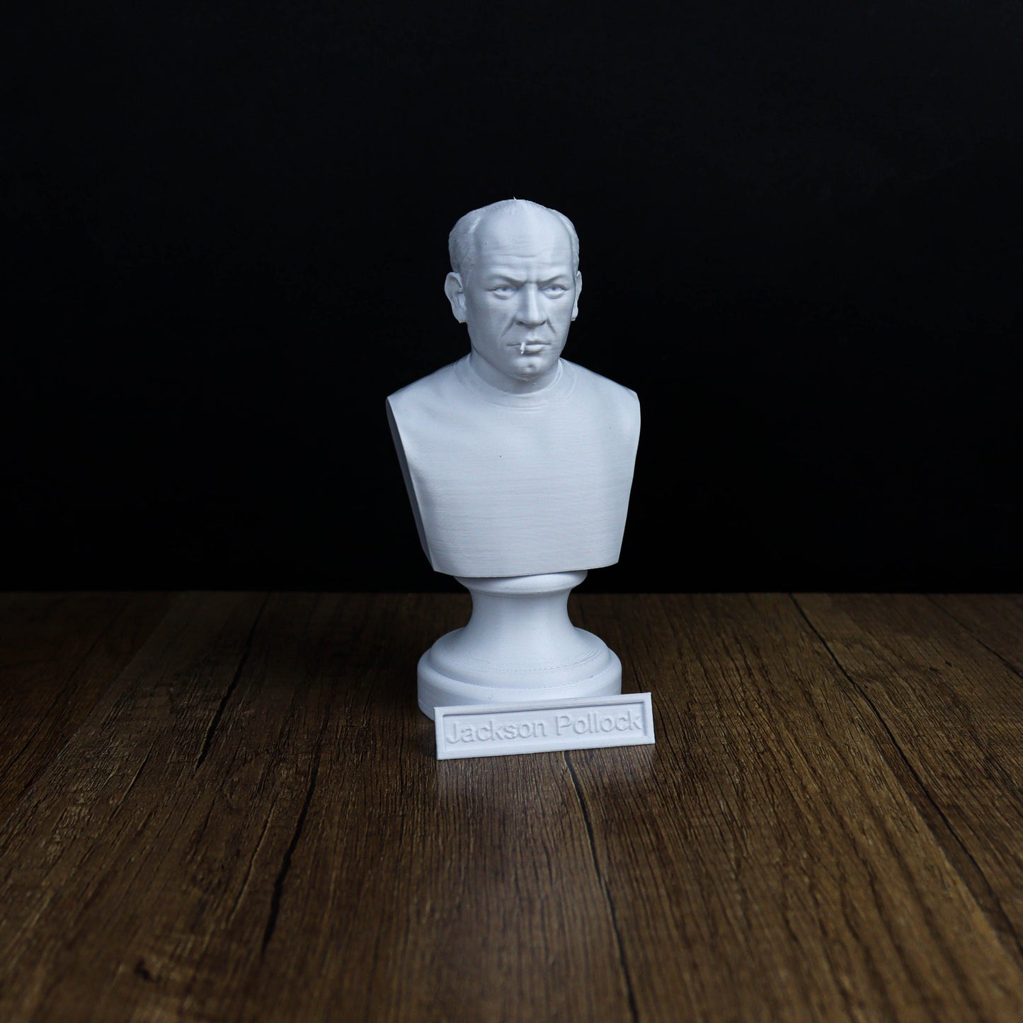 A white bust of a person is displayed on a wooden surface, with a small plaque in front of it that reads "Jackson Pollock".
