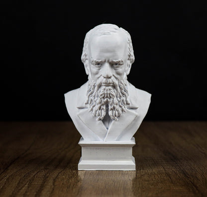 A white bust of a bearded man with a serious expression, sitting on a wooden surface against a black background.