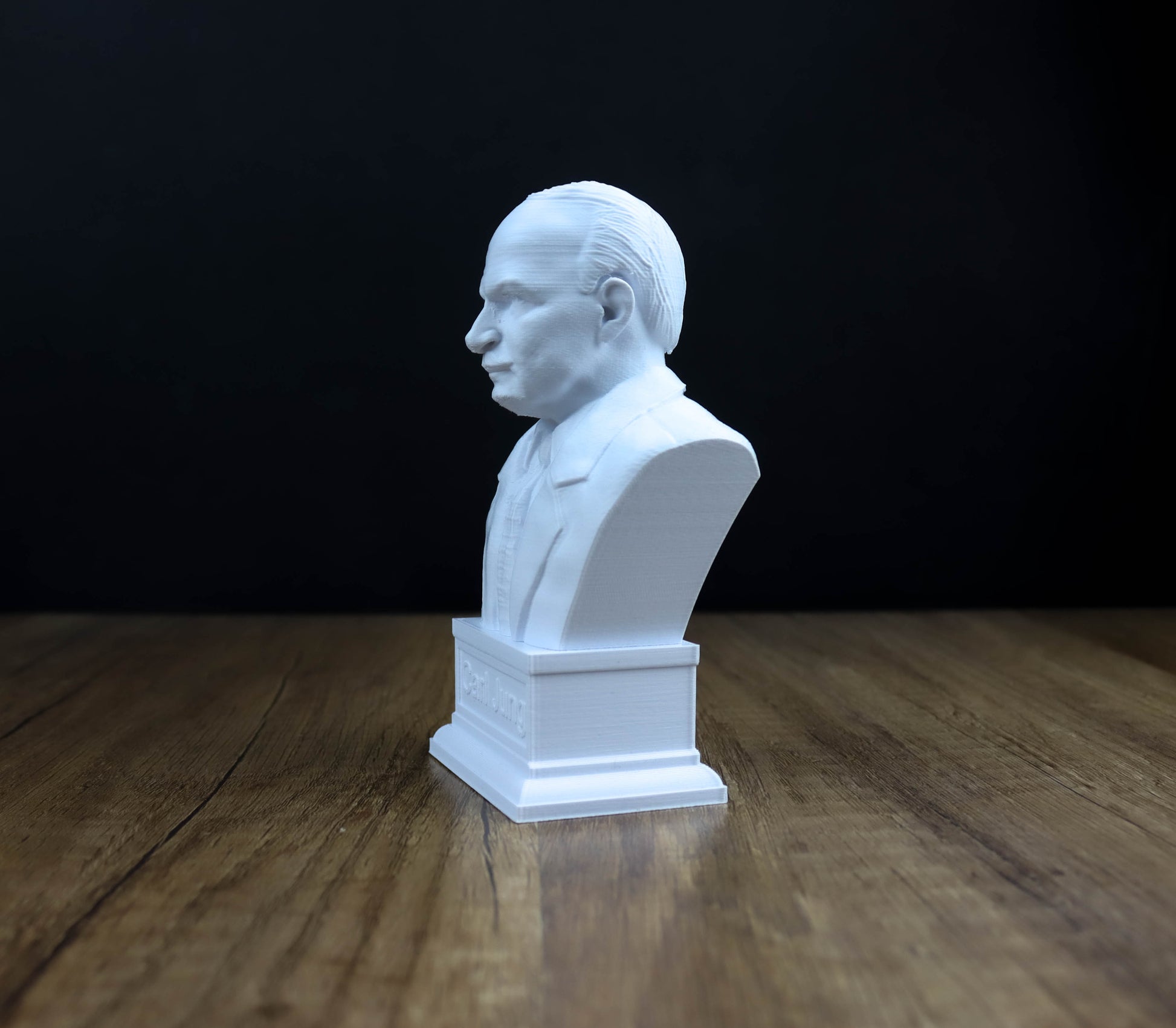 A white bust of a man is displayed on a wooden surface against a dark background.