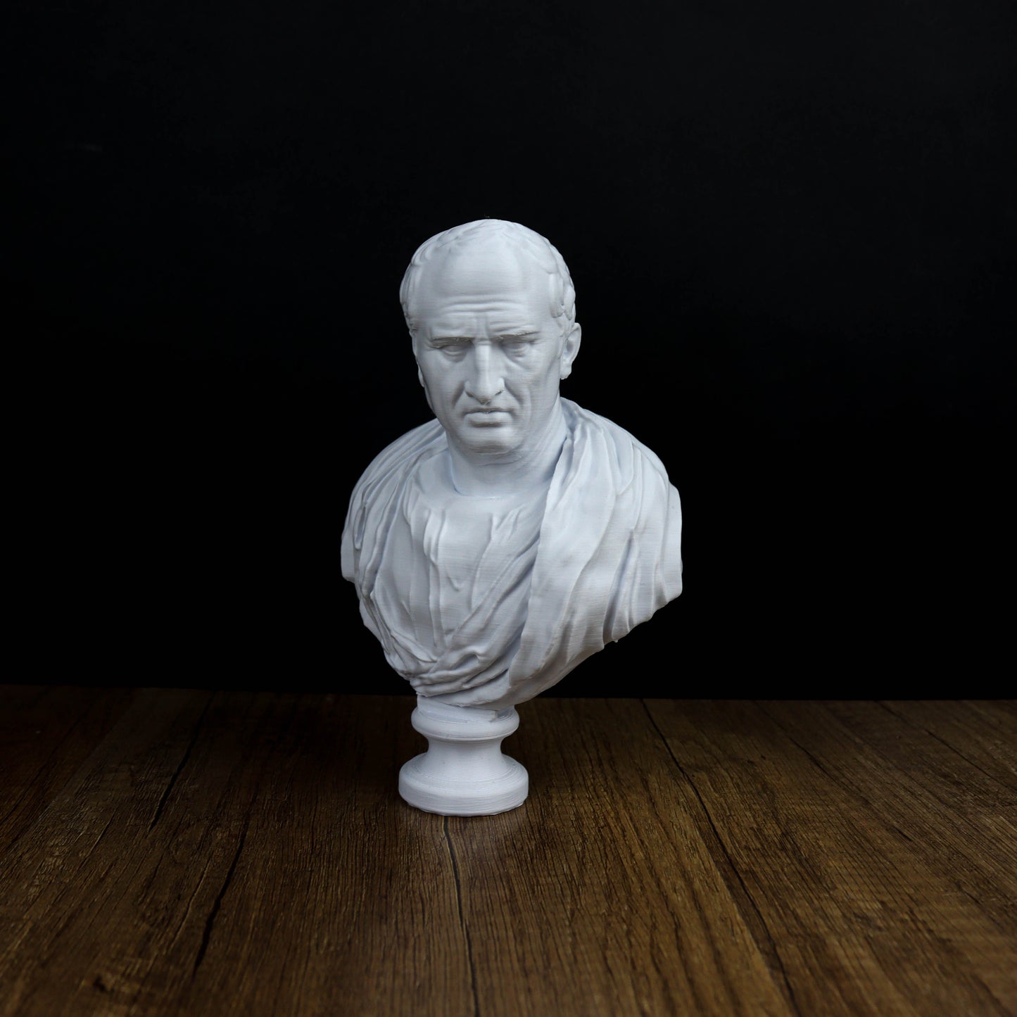 A white bust of a man is displayed on a wooden surface against a black background.