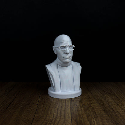 A white bust of a man wearing glasses is displayed on a wooden surface against a black background.