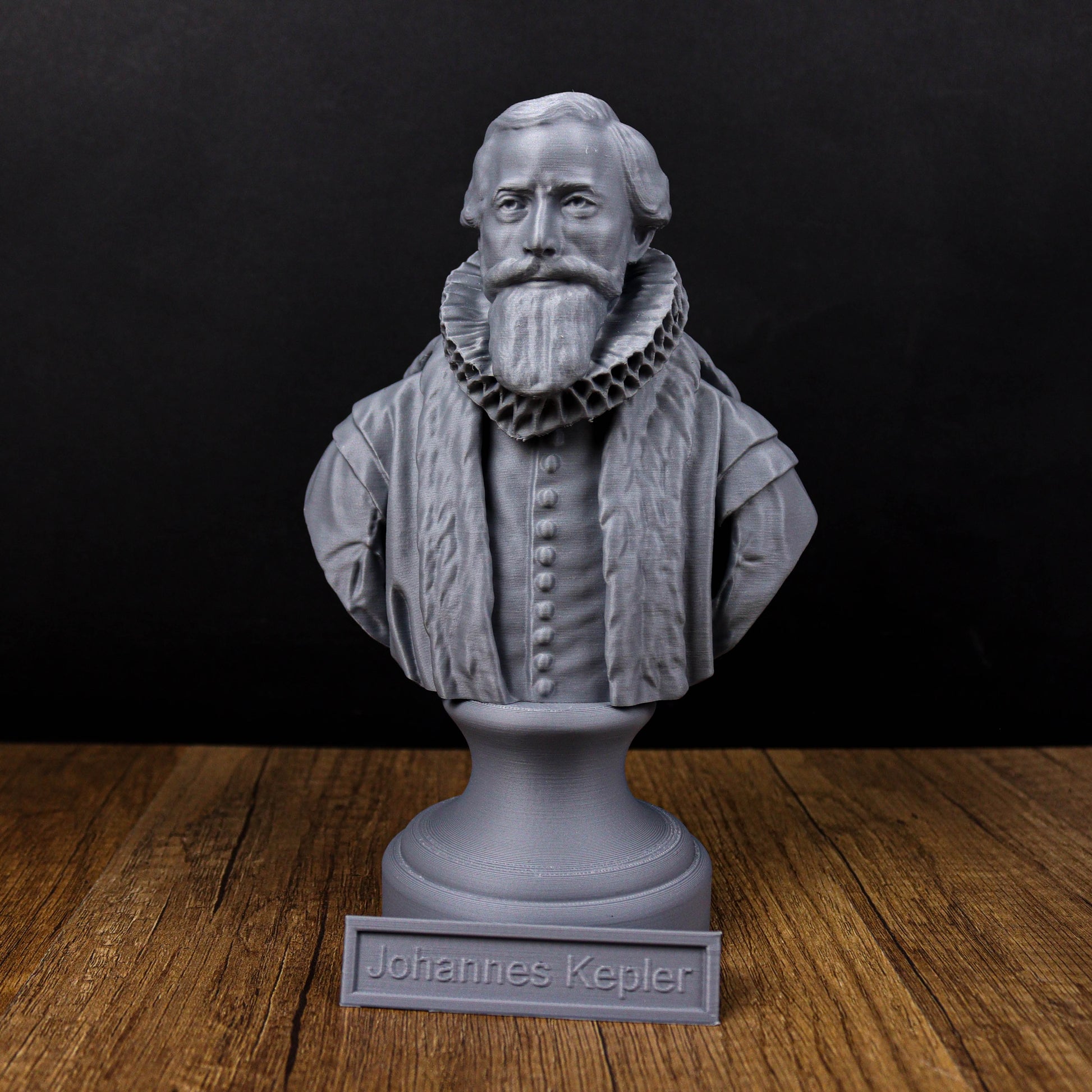 A bust of a bearded man wearing a ruffled collar, possibly representing Johannes Kepler, is displayed on a wooden surface.
