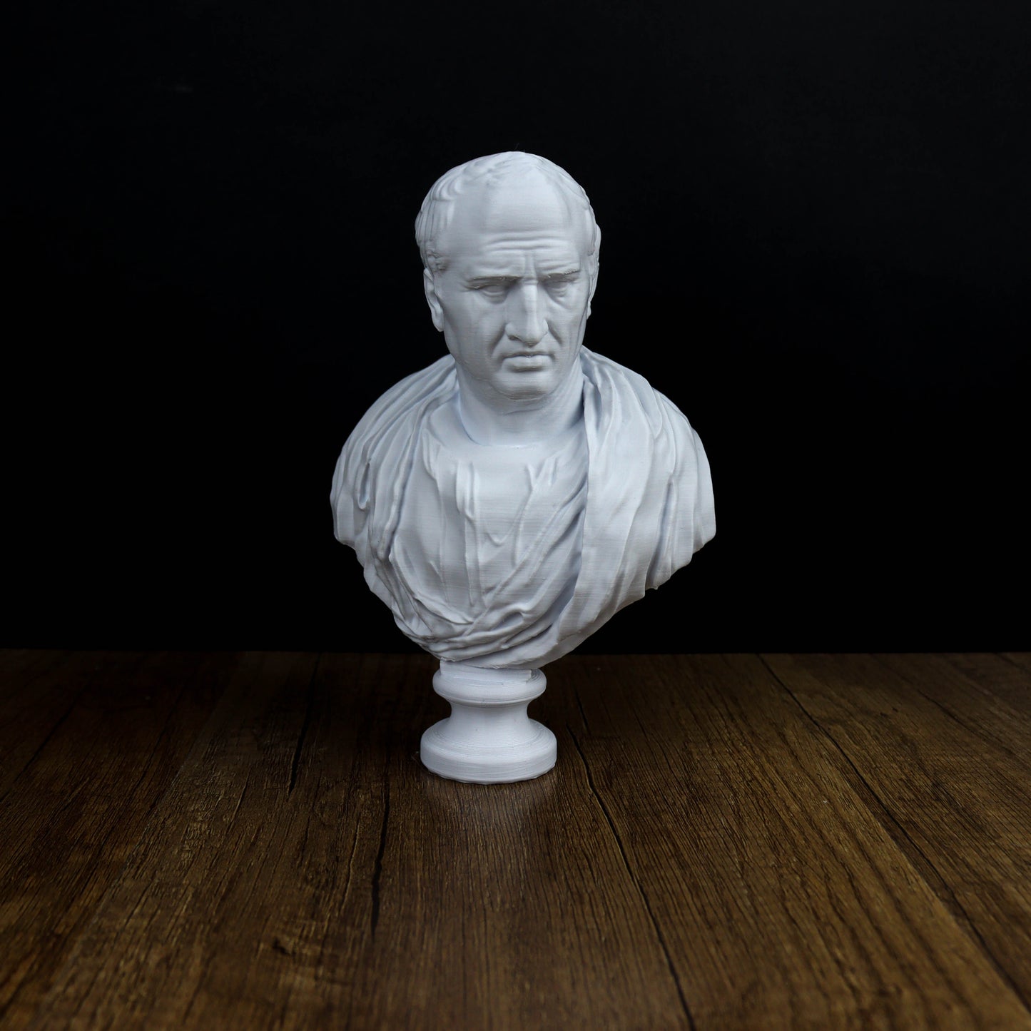 A white bust of a man is displayed on a wooden surface against a black background.