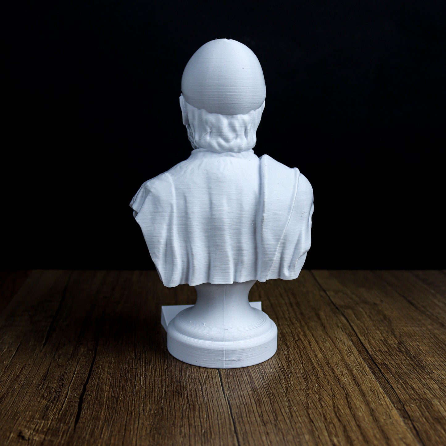 A white bust sculpture is displayed on a wooden surface against a dark background.
