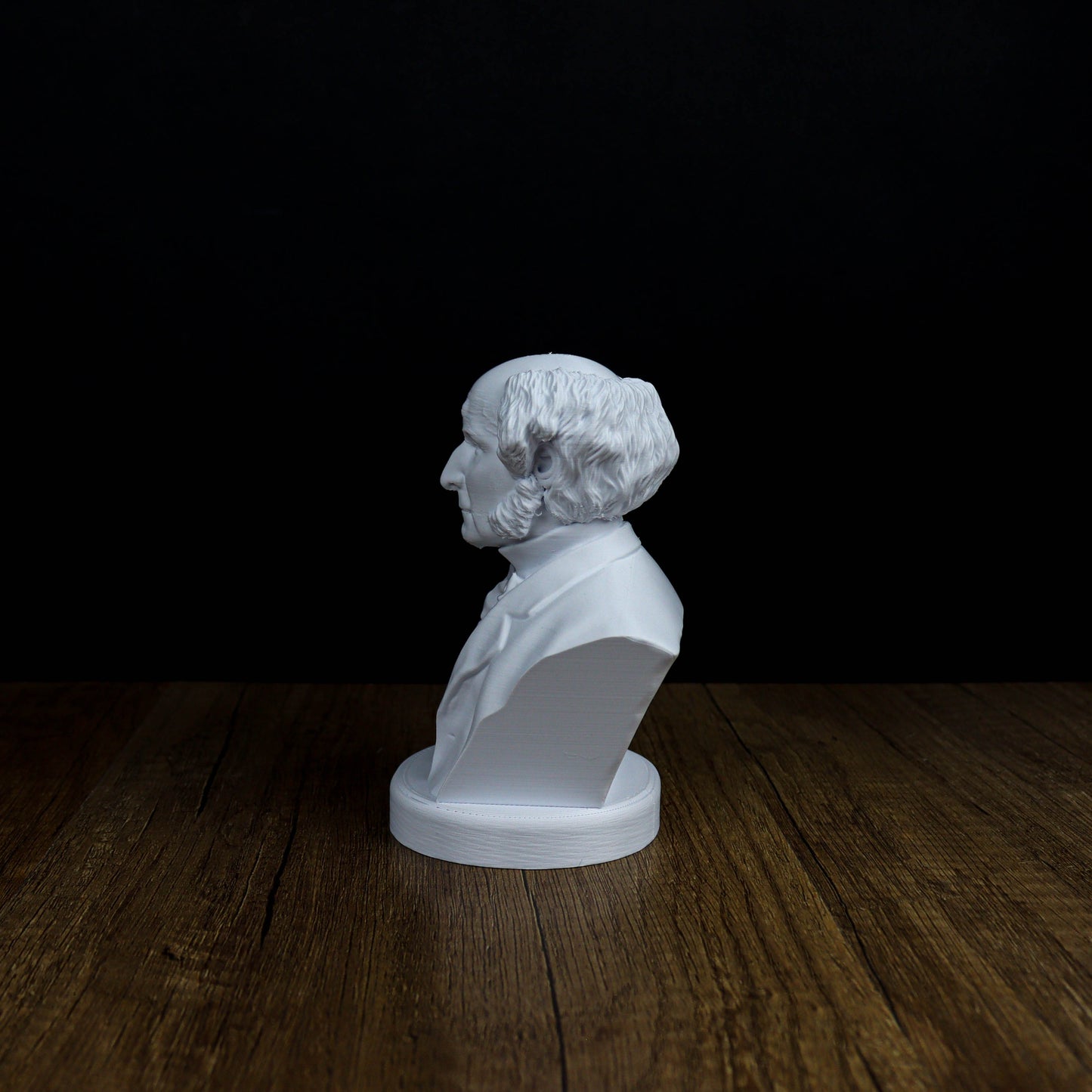 A white bust of a man with curly hair is displayed on a wooden surface against a black background.