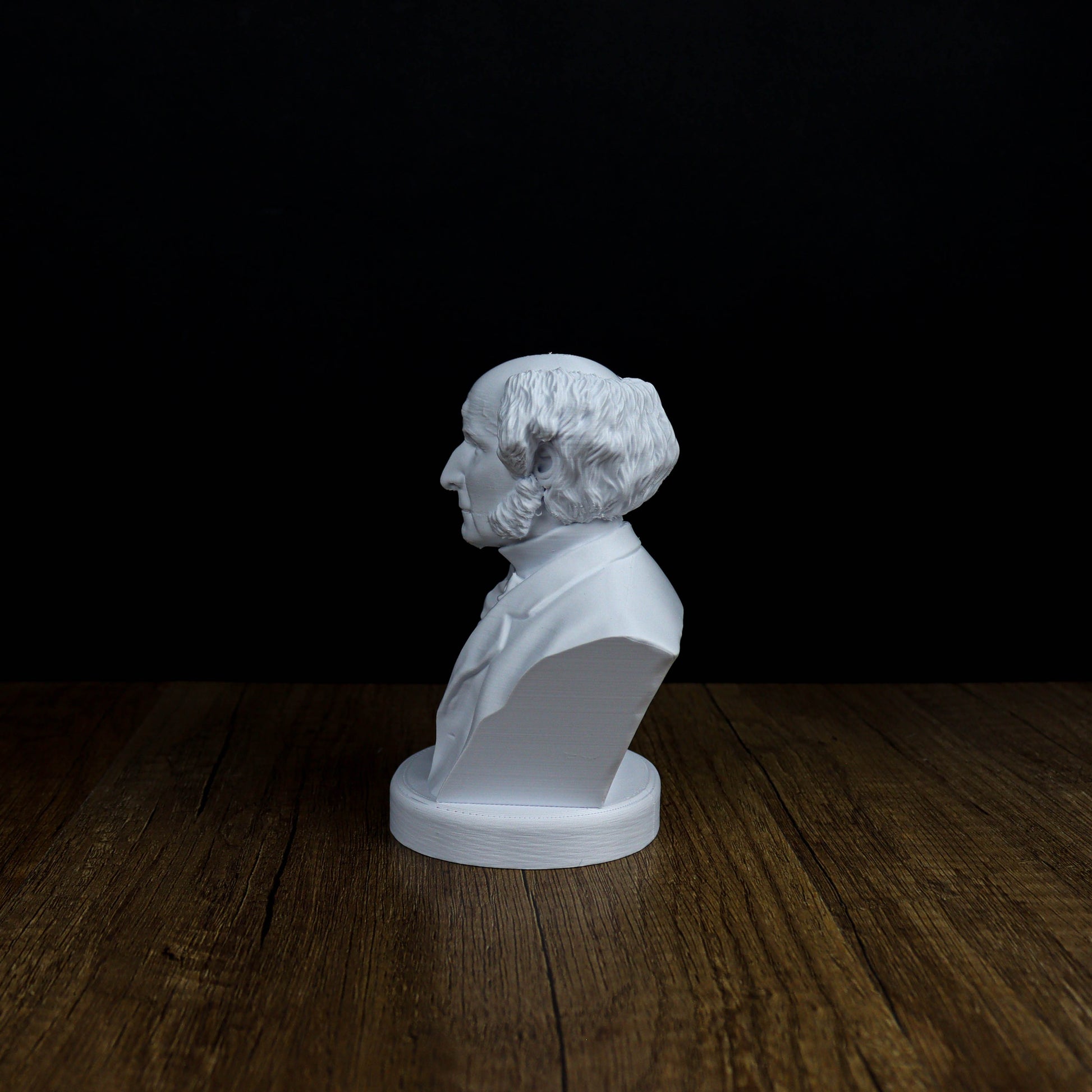 A white bust of a man with curly hair is displayed on a wooden surface against a black background.