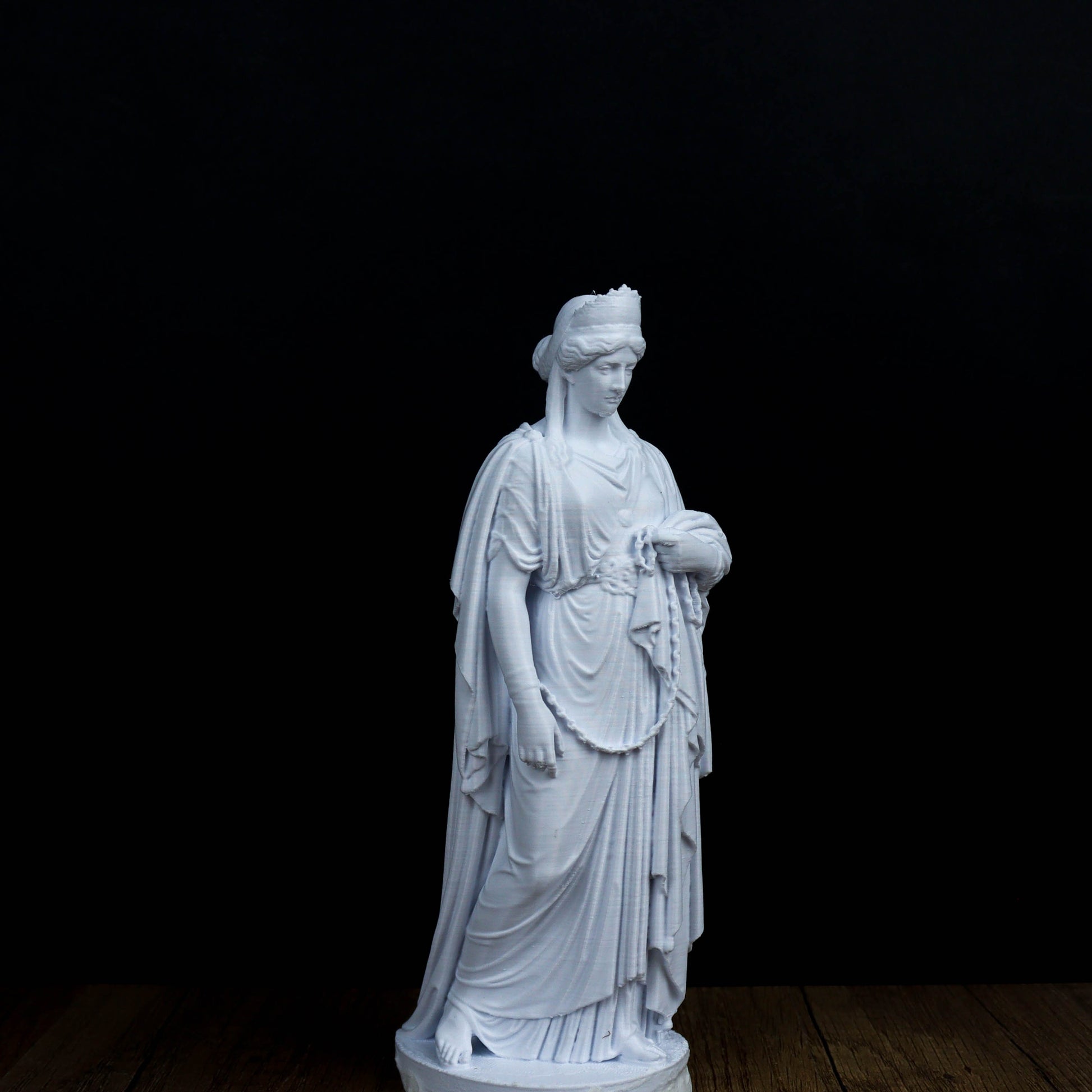 A white marble statue of a woman with a flowing robe and headdress stands against a black background.