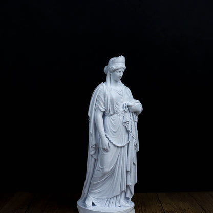 A white marble statue of a woman with a flowing robe and headdress stands against a black background.