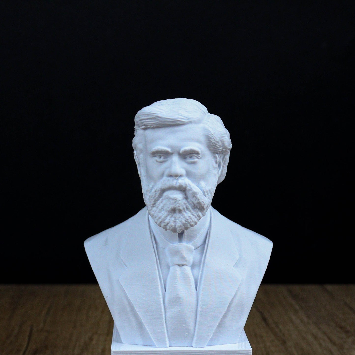 A white bust sculpture of a man with a beard and mustache, wearing a suit and tie, is displayed against a black background.