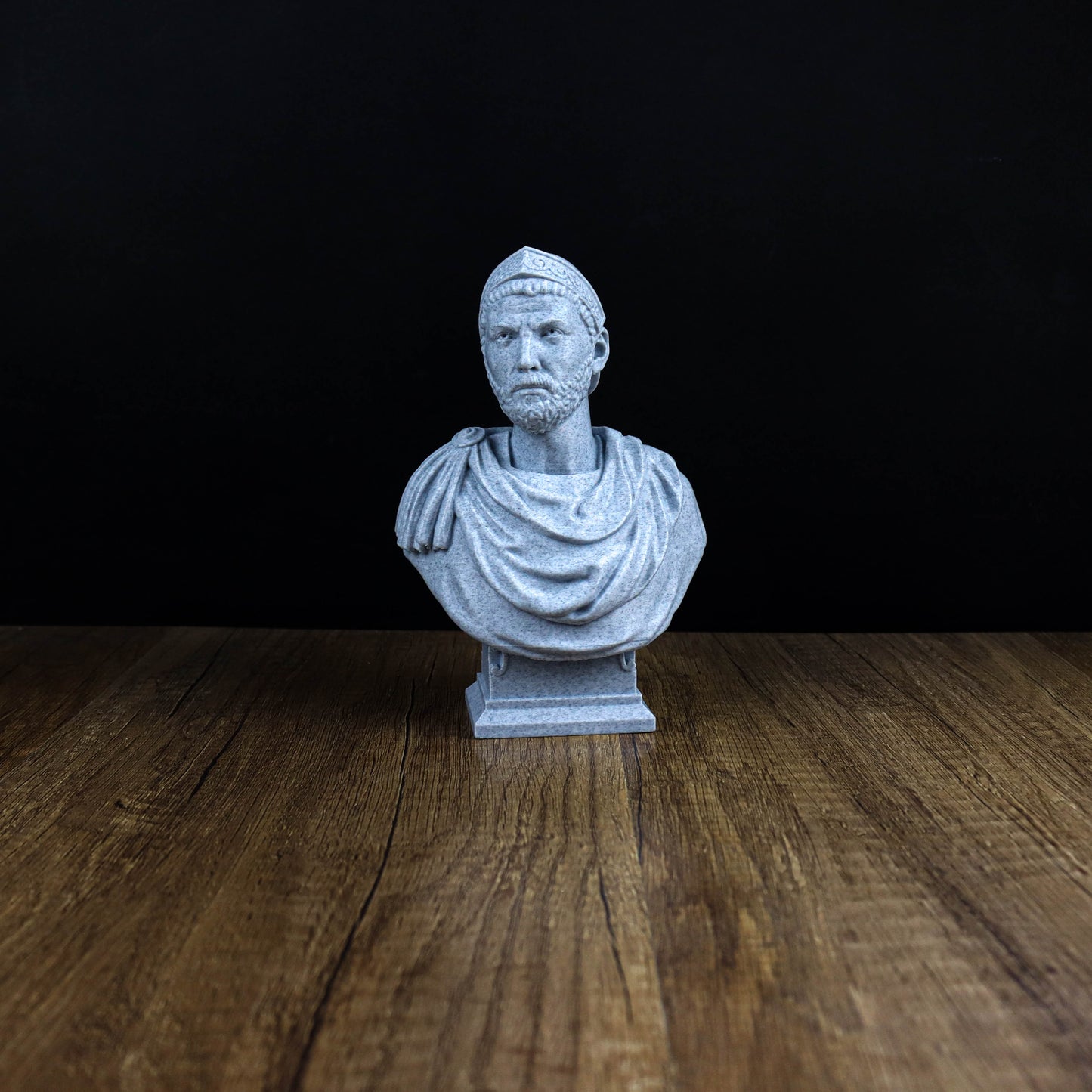 A small white bust of a man is displayed on a wooden surface against a black background.