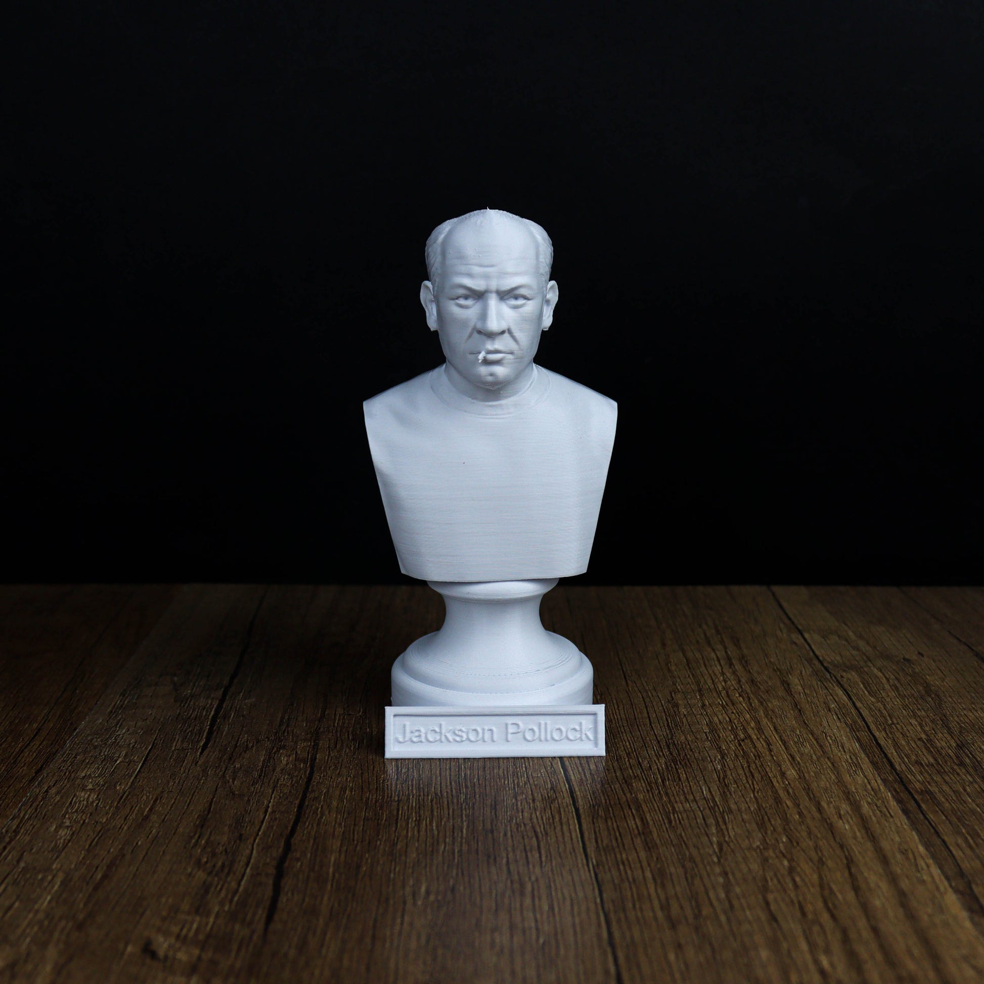 A white bust of a man's head is displayed on a wooden surface against a black background.
