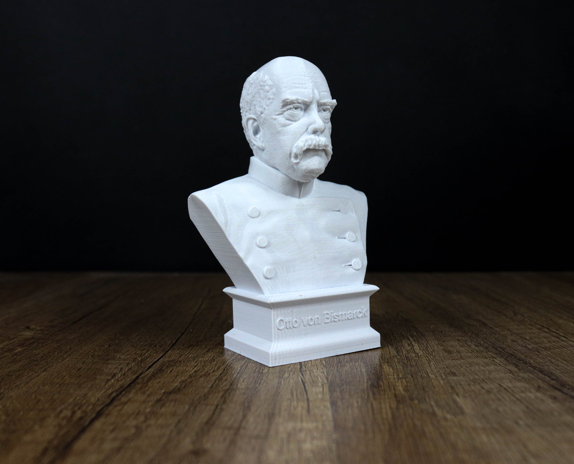 A white bust of a man with a mustache and a military-style uniform, sitting on a wooden surface.