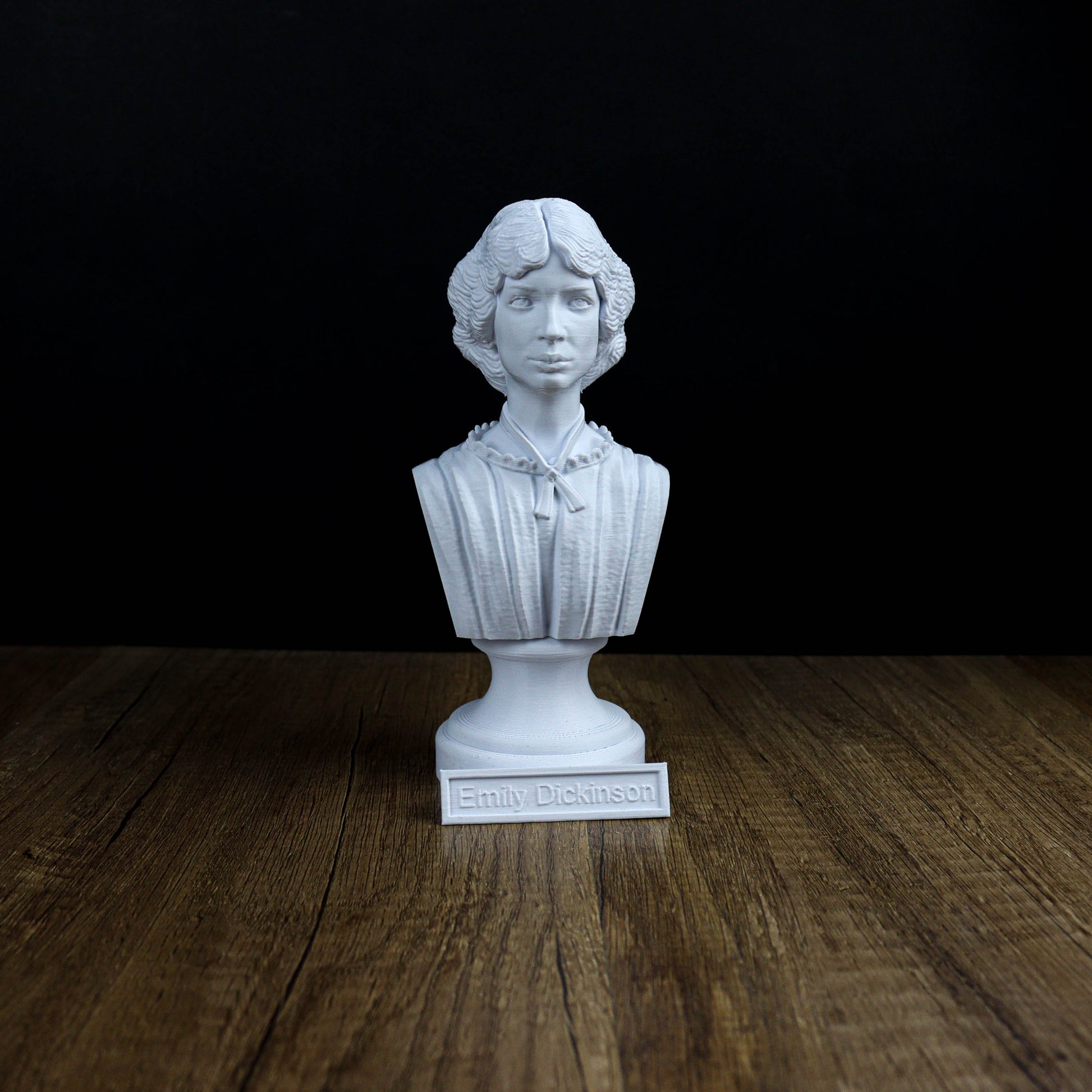 A white bust of a person, likely a historical figure, is displayed on a wooden surface against a black background.