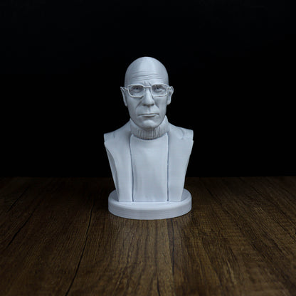 A white bust of a man wearing glasses is displayed on a wooden surface against a black background.