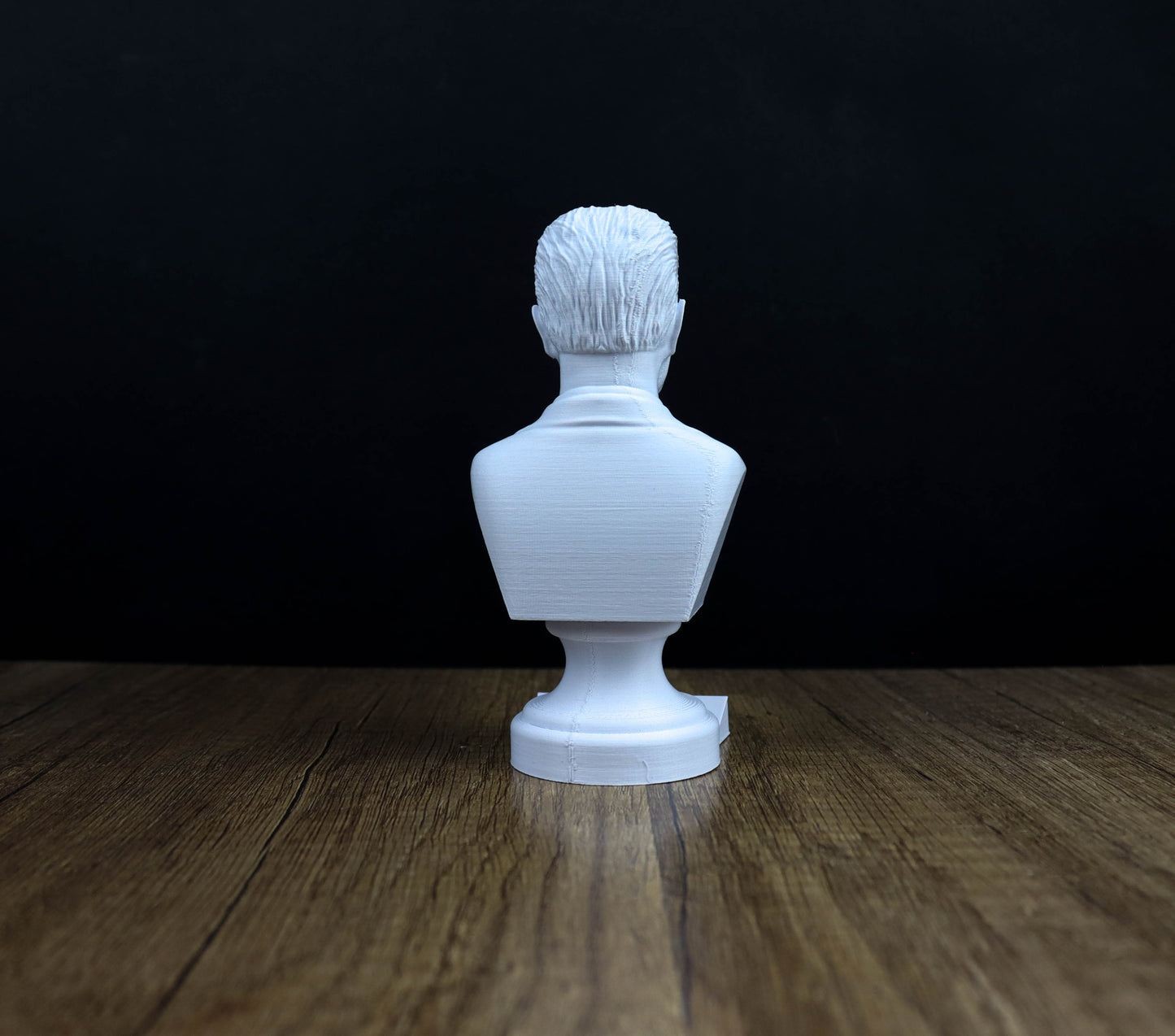 A white bust of a person is sitting on a wooden surface against a dark background.