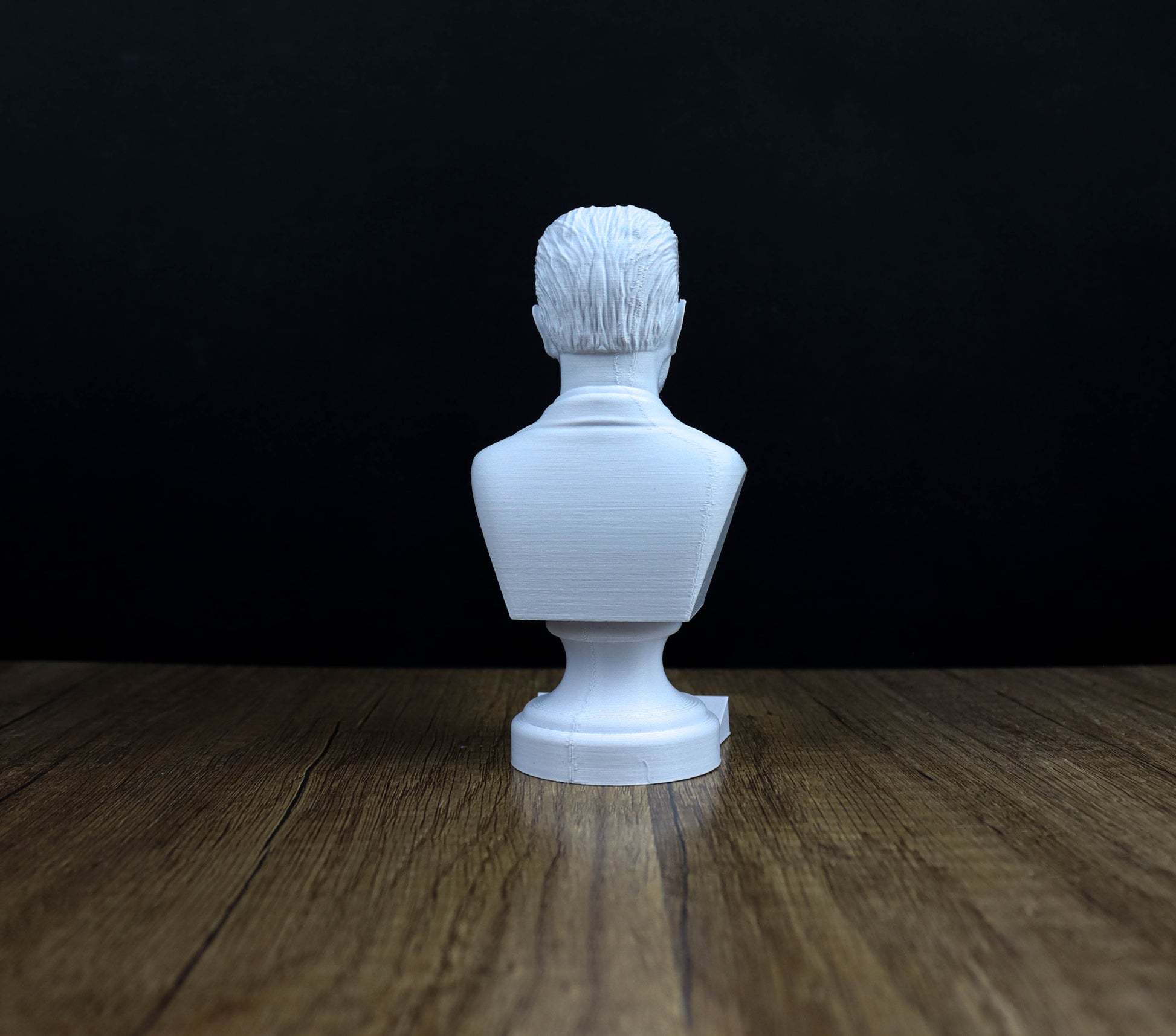 A white bust of a person is sitting on a wooden surface against a dark background.
