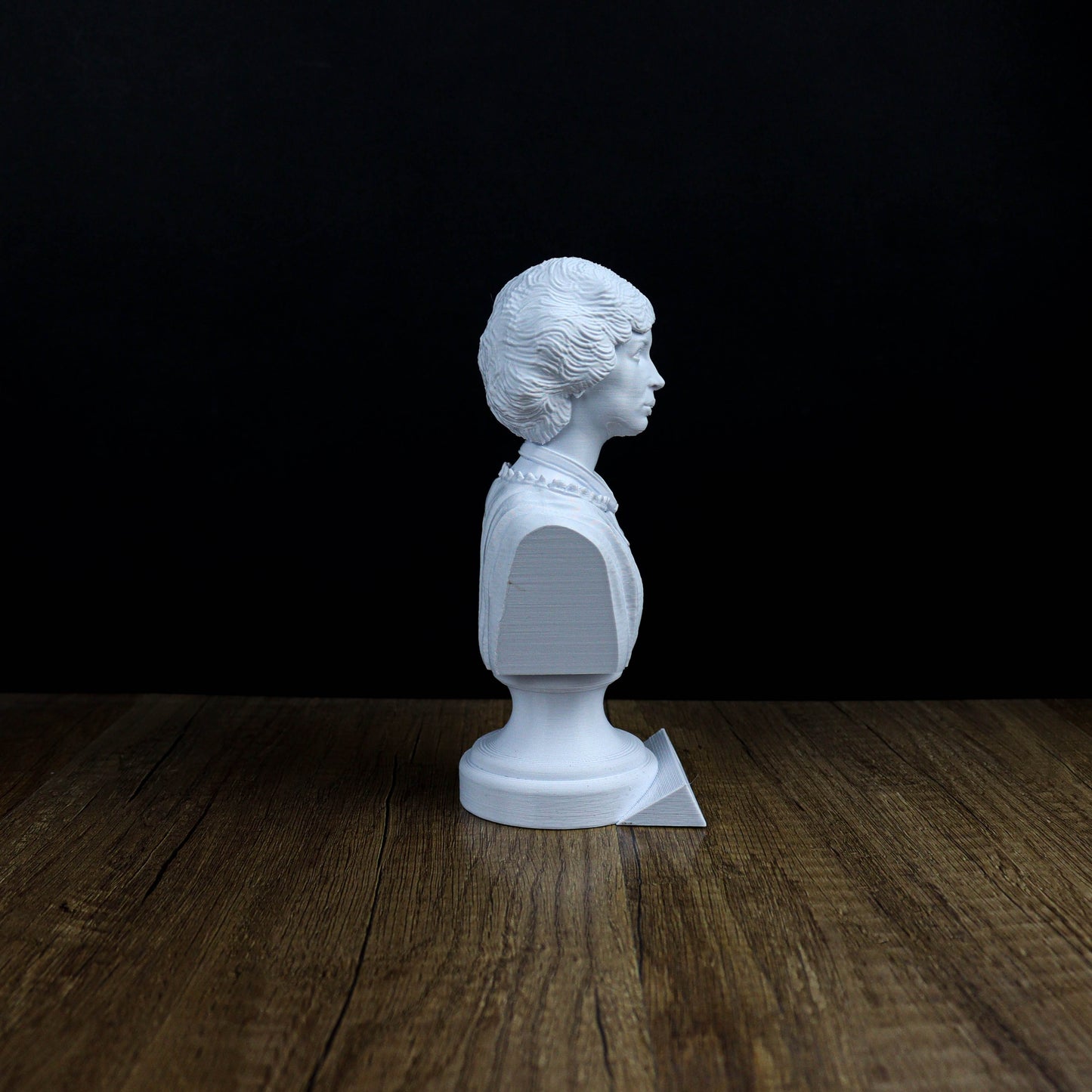 A white bust of a person is sitting on a wooden surface against a black background.