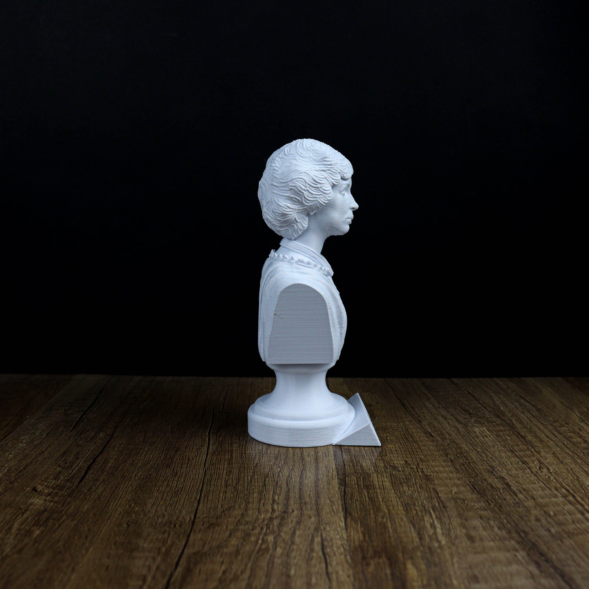 A white bust of a person is sitting on a wooden surface against a black background.
