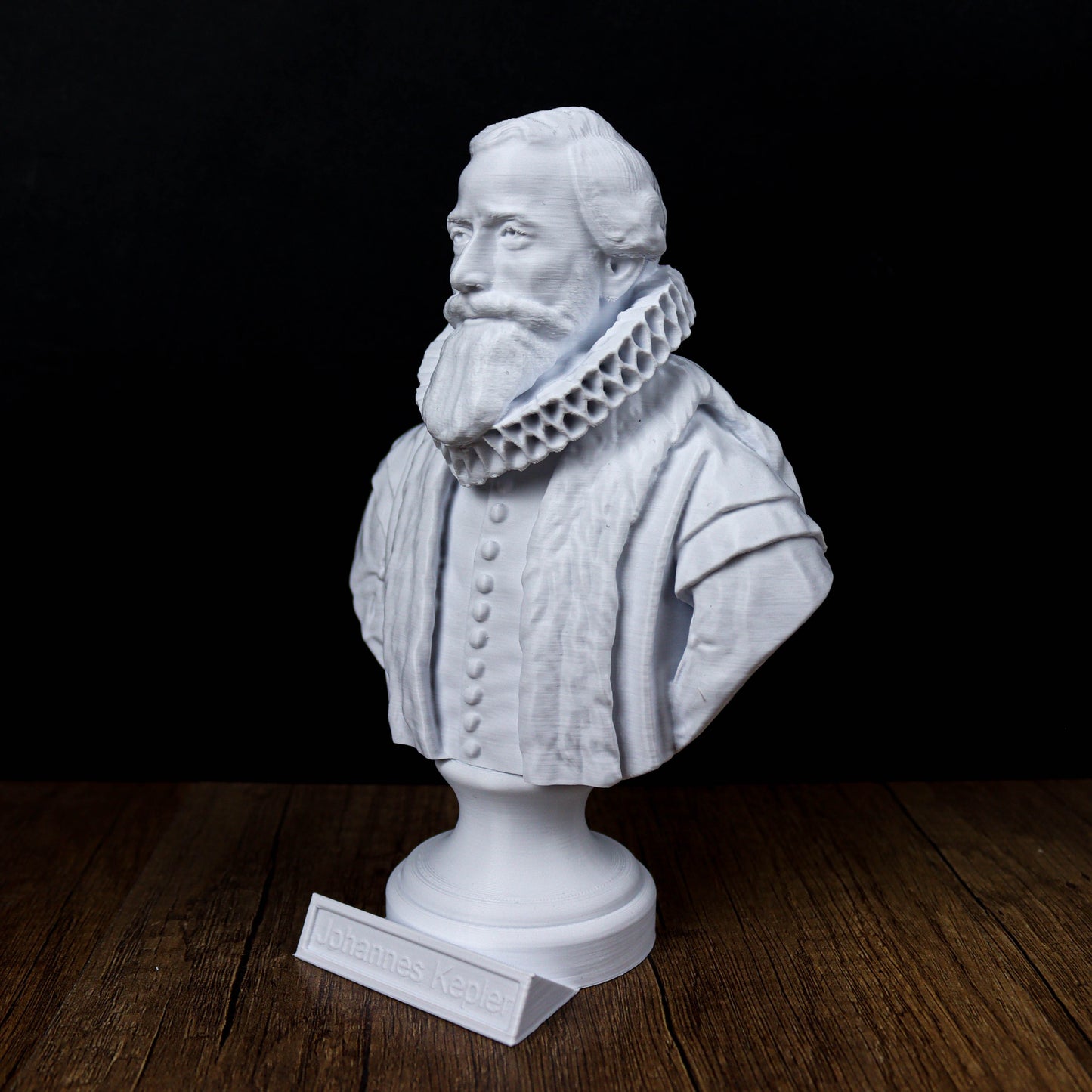 A white bust of a bearded man wearing a ruffled collar, placed on a wooden surface.