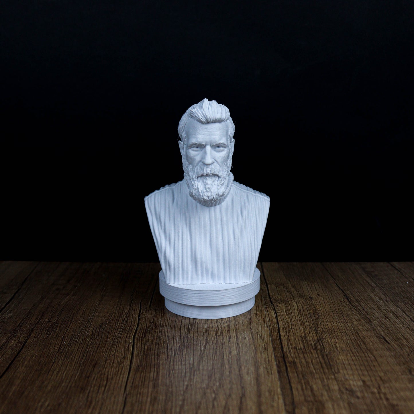 A white bust of a bearded man is displayed on a wooden surface against a dark background.