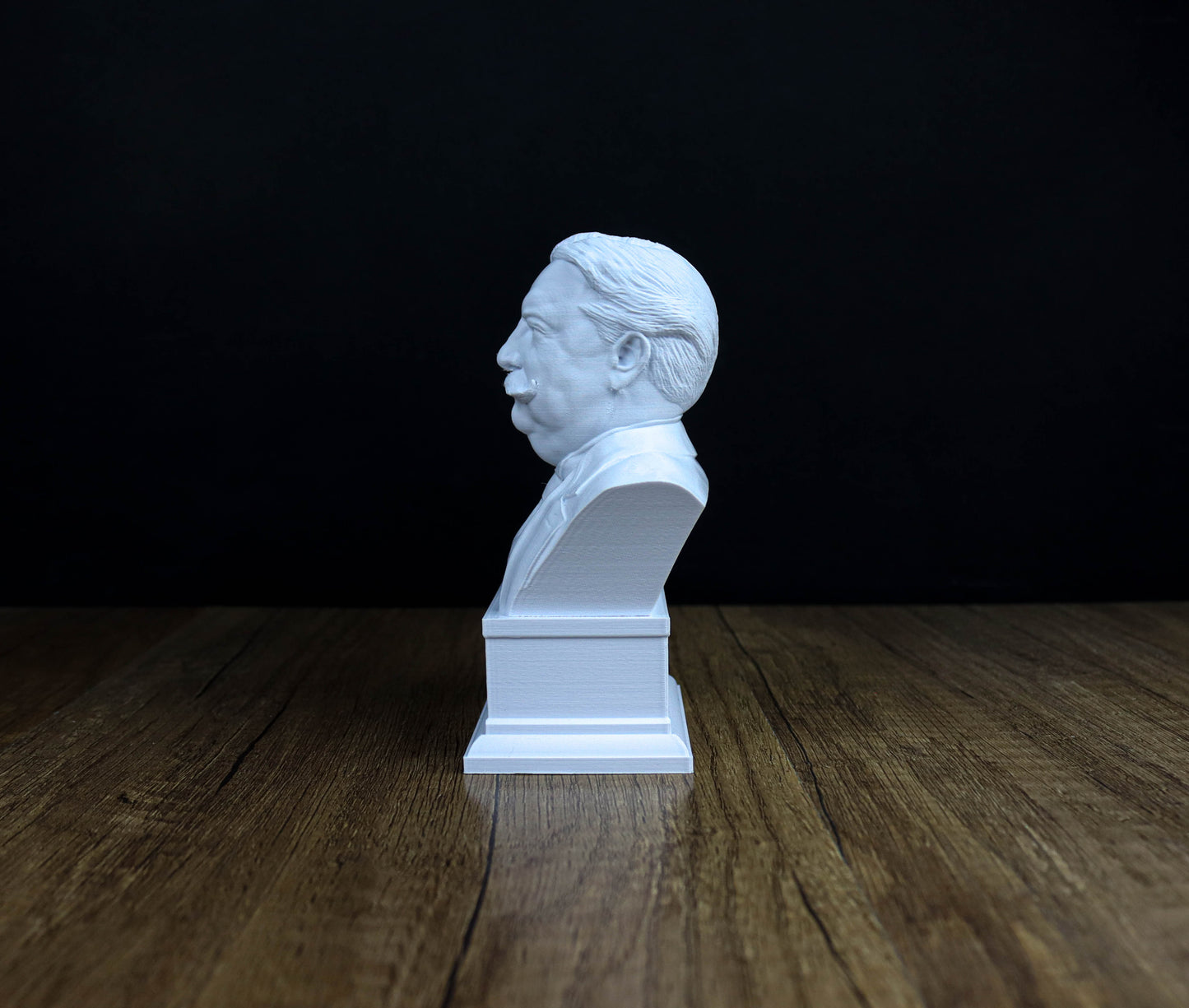 A white bust of a man is sitting on a wooden surface against a dark background.
