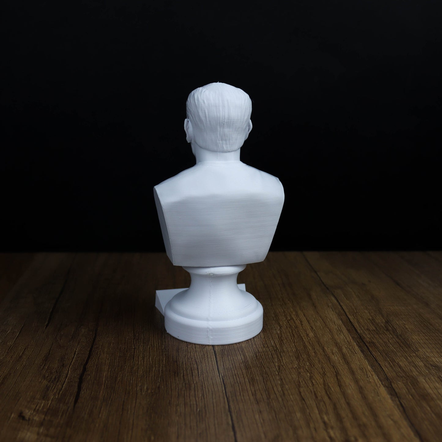 A white bust sculpture is sitting on a wooden surface against a dark background.