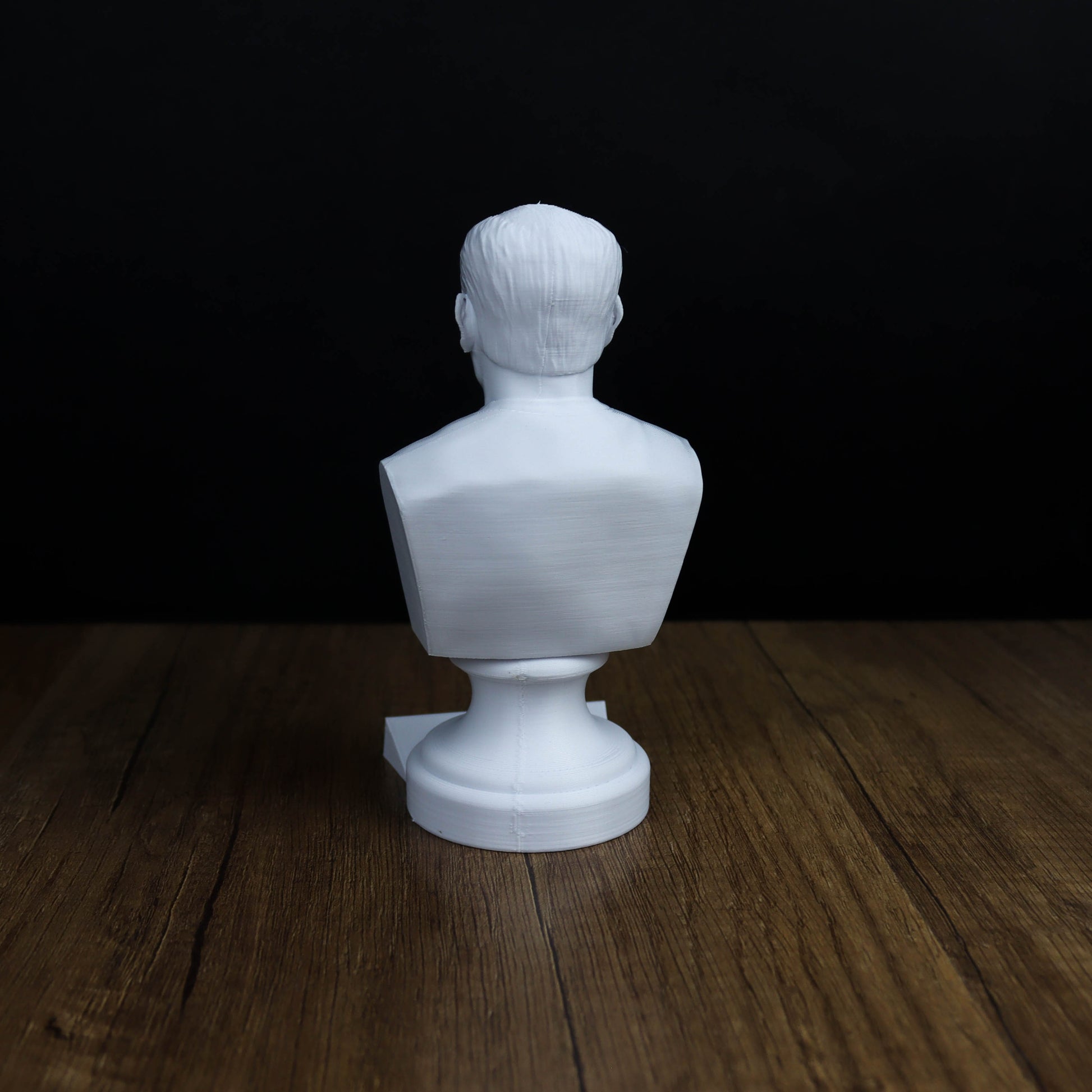 A white bust sculpture is sitting on a wooden surface against a dark background.